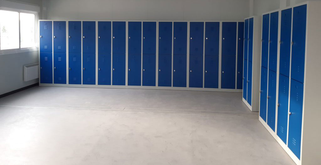 Une affiche de sécurité plastifiée est visible sur le mur d'un vestiaire industriel avec des casiers métalliques en arrière-plan